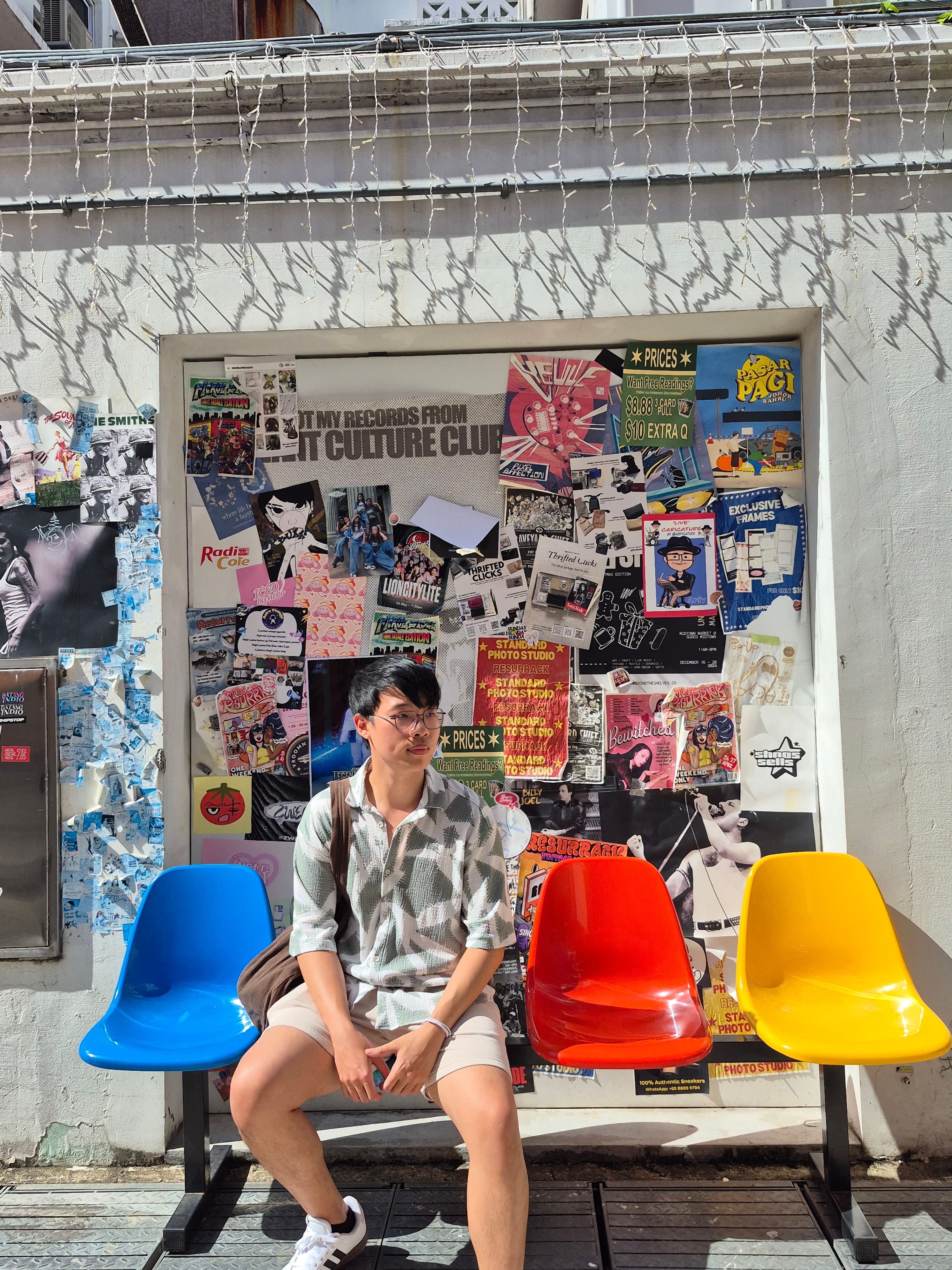Kah Ho sitting on colourful chairs in front of a poster wall